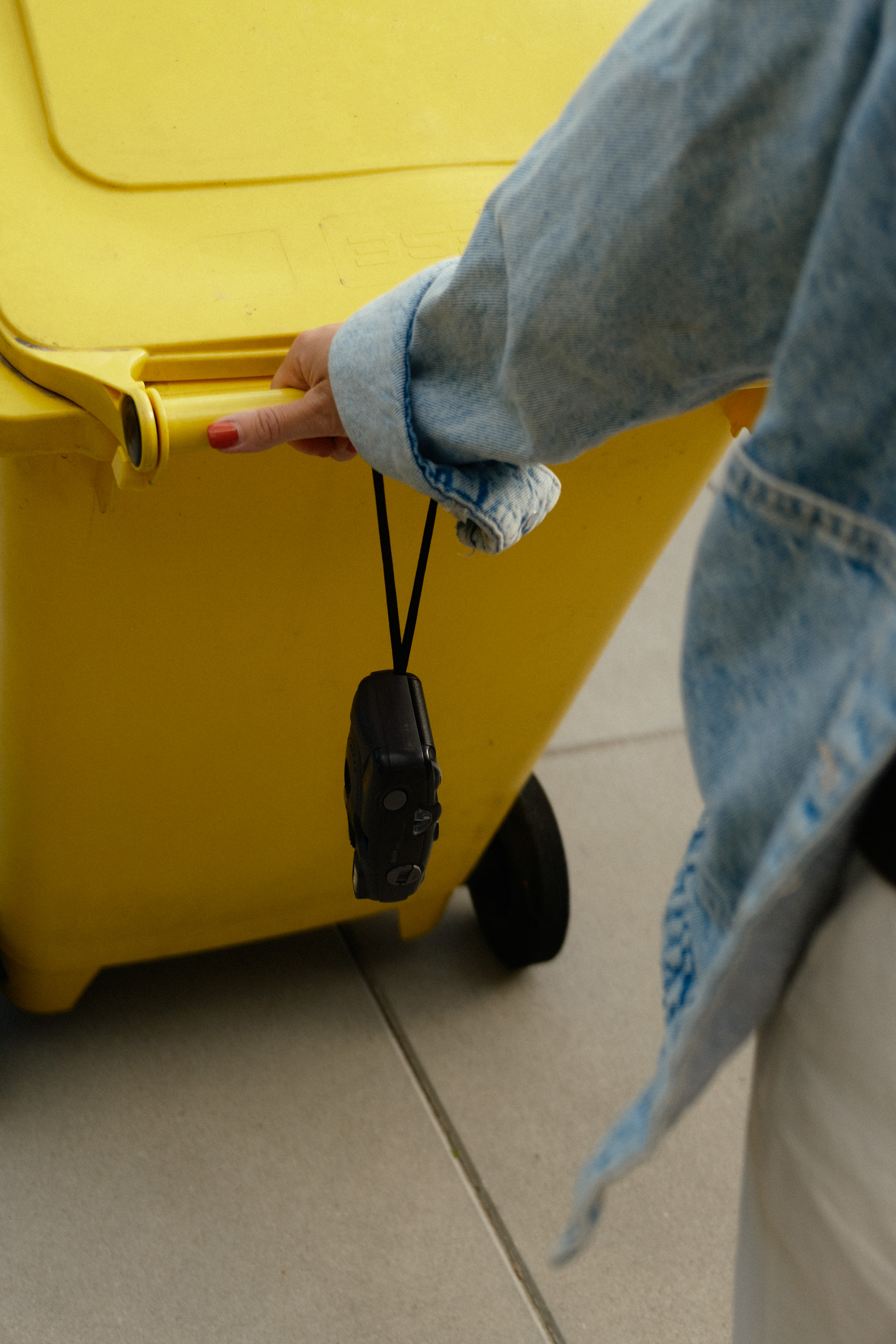 main tirant une poubelle jaune de recyclage avec un appareil photo au poignée